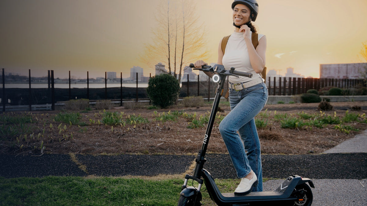 Mujer ajustándose el casco junto a su scooter eléctrico al atardecer - E-Mobility Chile, Las Condes