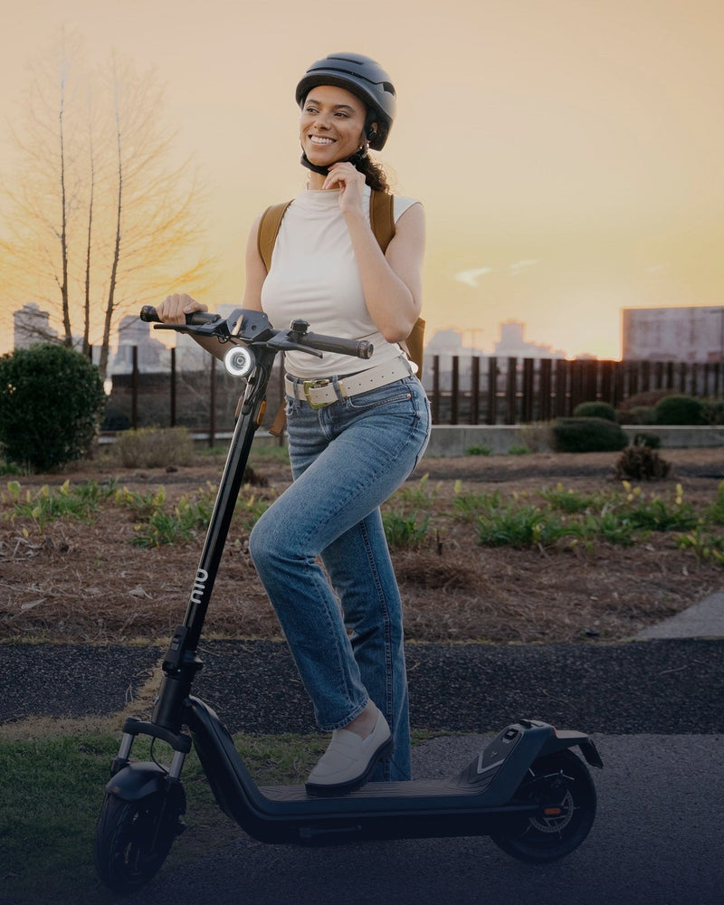 Mujer ajustándose el casco junto a su scooter eléctrico al atardecer - E-Mobility Chile, Las Condes